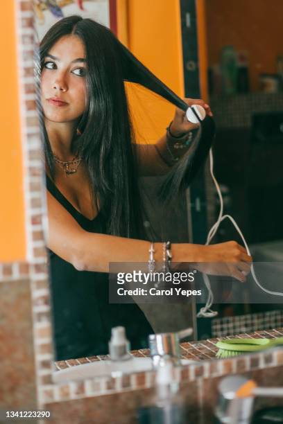 woman using hair straightener at home before going out for dinner - hair part stock-fotos und bilder