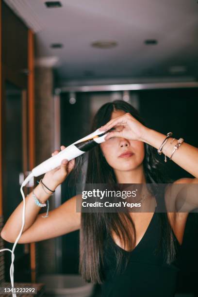 woman using hair straightener at home - haircare stockfoto's en -beelden