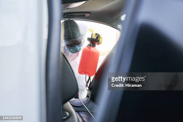 foto de un hombre con un traje de materiales peligrosos usando un pulverizador químico para desinfectar un automóvil - crime scene cleaners fotografías e imágenes de stock