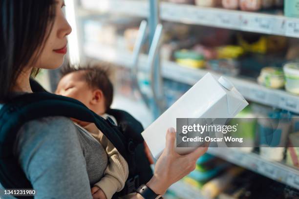 cropped shot of young mother doing grocery shopping with her baby daughter in a carrier at supermarket - mom buying milk stock pictures, royalty-free photos & images