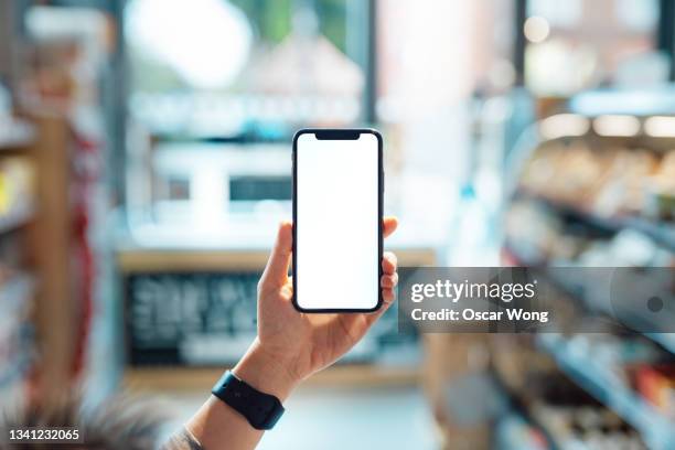 smart phone with blank screen held up in supermarket - hand holding phone stockfoto's en -beelden