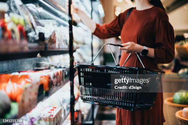 cropped shot of young woman carrying a shopping basket, standing along the product aisle, grocery shopping for daily necessities in supermarket - aisle stock-fotos und bilder