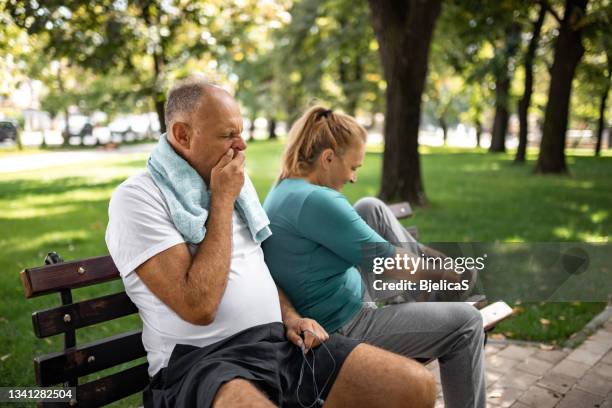 mature couple relaxing after jogging together in public park - yawning stock pictures, royalty-free photos & images