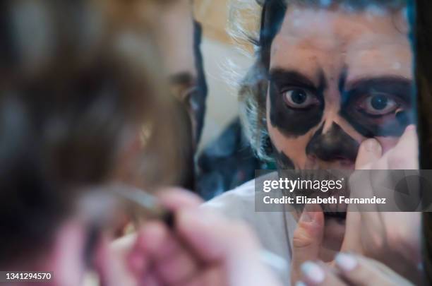 young man applying halloween makeup at home, his girlfriend holding the mirror - halloween zombie makeup imagens e fotografias de stock