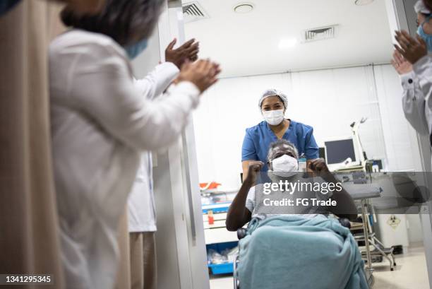 doctors and nurses celebrating senior man leaving the hospital after recovery - wearing protective face mask - applauding nurses stock pictures, royalty-free photos & images