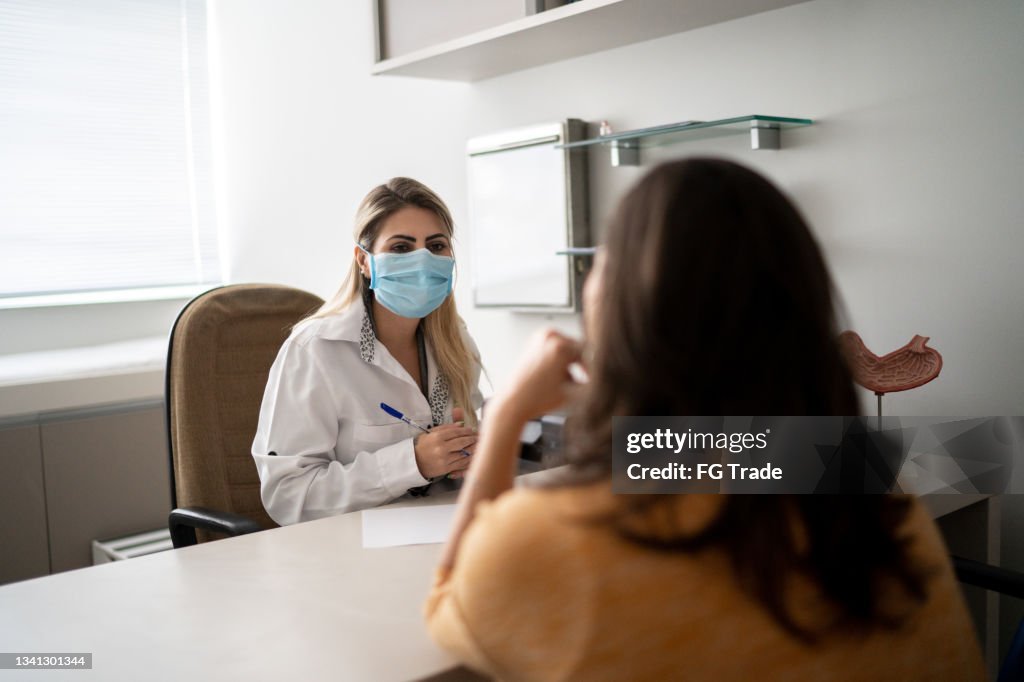 Doctor talking to patient on medical appointment - wearing protective face mask