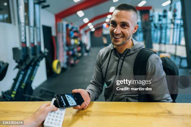man in the gym paying with smart phone - gym receptionist stock pictures, royalty-free photos & images