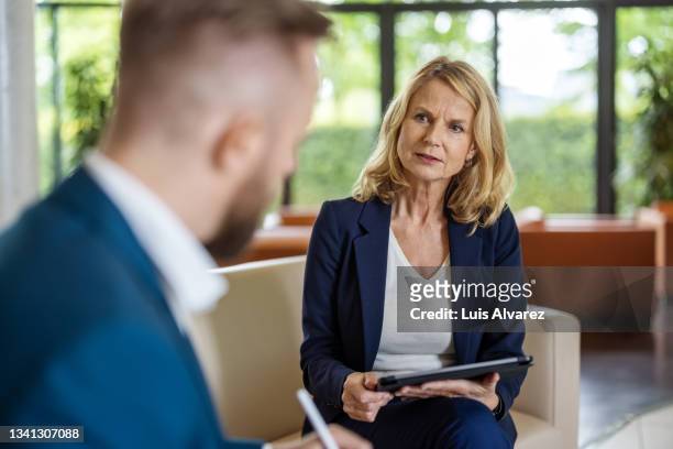 senior businesswoman having meeting with a colleague in office lobby - blue blazer stock pictures, royalty-free photos & images