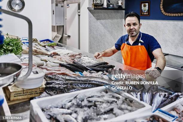 caucasian worker at seafood market wearing orange apron and preparing fresh fish display. small business and food concept - fish market stock pictures, royalty-free photos & images