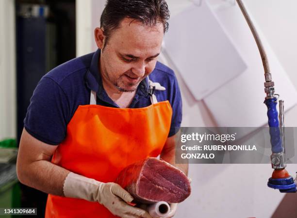 fishmonger wearing an orange apron holding and wrapping a piece of tuna at fish market - man wrapped in plastic stock pictures, royalty-free photos & images