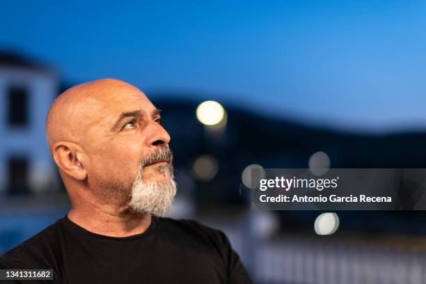 mature 60-year-old man is portrayed at nightfall during blue hour with traffic lights in the background - handsome 50 year old men imagens e fotografias de stock