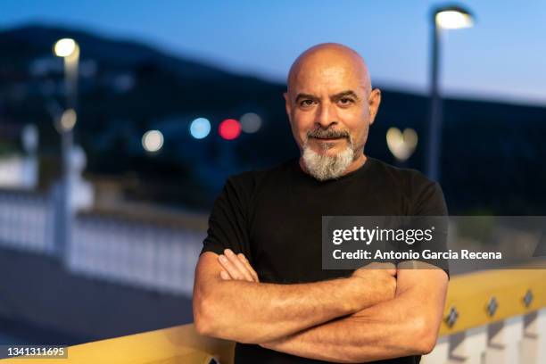 mature 60-year-old man is portrayed at nightfall during blue hour with traffic lights in the background - old arab man stock pictures, royalty-free photos & images