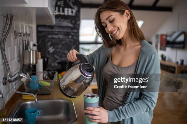 smiling woman standing in kitchen and pouring reusable travel mug with coffee - flask stock pictures, royalty-free photos & images