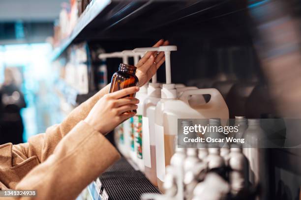 young woman refilling shower gel into a reusable glass bottle in zero waste store - sustainable cosmetics stock pictures, royalty-free photos & images