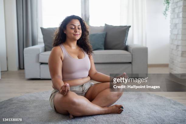portrait of beautiful young overweight woman indoors at home, doing meditation exercise. - fat asian woman stock pictures, royalty-free photos & images