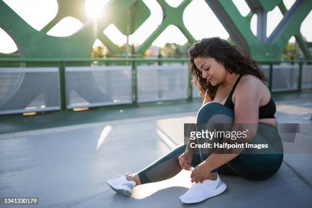 portrait of beautiful young overweight woman tying laces outdoors on bridge in city, resting after exercise. - fat asian woman stock pictures, royalty-free photos & images