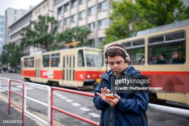 self sufficient young down syndrome man with headphones using smartphone outdoors in city street. - disabilitycollection fotografías e imágenes de stock