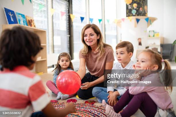 pre- school teacher sitting on floor and playing with children indoors in nursery. - bambini seduti in cerchio foto e immagini stock