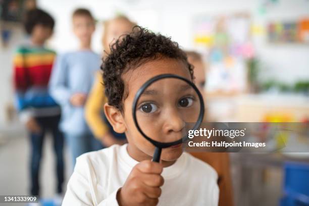 pre- school tboy playing with magnifying glass indoors at nursery school, looking at camera. - child magnifying glass stock pictures, royalty-free photos & images