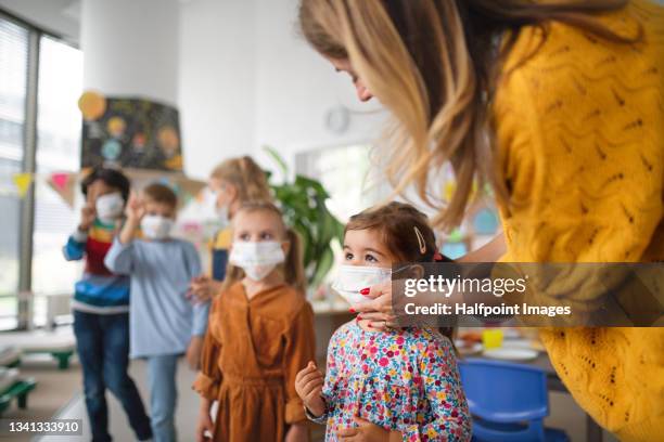 pre - school teacher help children to wear face masks indoors at nursery school, coronavirus concept. - teacher pre school bildbanksfoton och bilder
