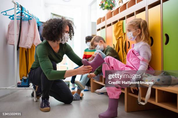pre school teacher helping little girl put on shoes indoors in cloakroom at nursery, coronavirus concept. - young boys changing in locker room 個照片及圖片檔