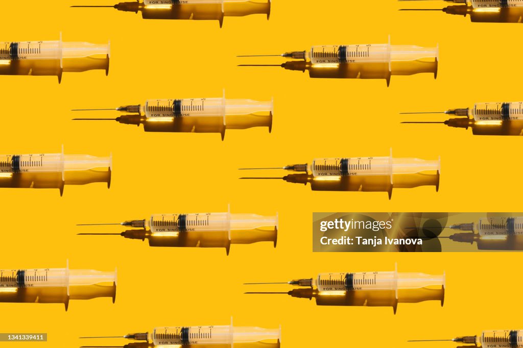 Pattern of syringes with a vaccine on yellow background. Concept of medical treatment or vaccination.