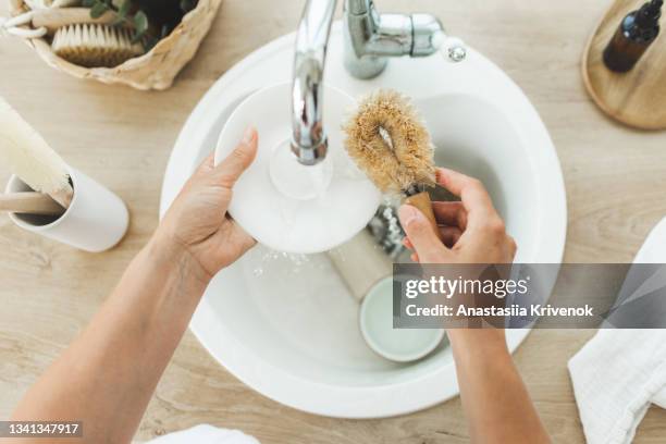 woman housemaid uses a wooden brush to clean dishes in a kitchen sink. - loofah stock pictures, royalty-free photos & images