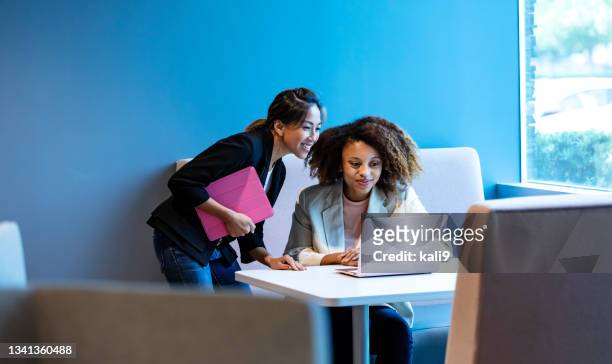 two multiracial women look at laptop in office work area - filipino woman smiling stock pictures, royalty-free photos & images