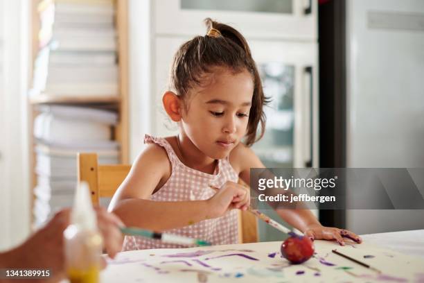 foto de una niña pintando huevos en casa - petite latina fotografías e imágenes de stock