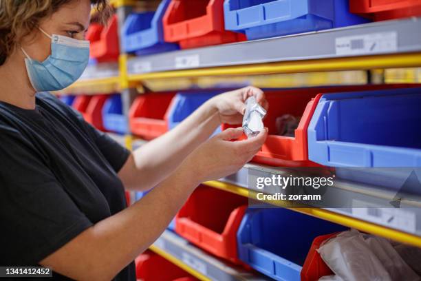 warehouse worker holding an item from storage trays in a row on racks - industrial storage bins stockfoto's en -beelden