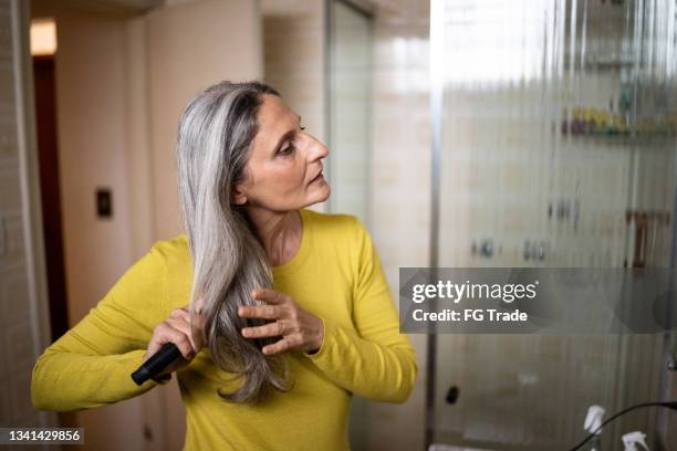 reife frau, die sich zu hause die haare bürstet - haare kämmen stock-fotos und bilder