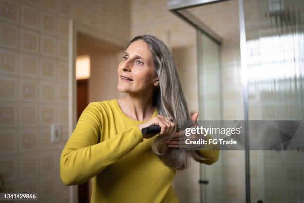 reife frau, die sich zu hause die haare bürstet - brushing hair stock-fotos und bilder