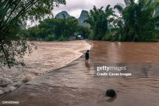 man crossing flooded road, yangshuo, guangxi province, china - east asia stock pictures, royalty-free photos & images