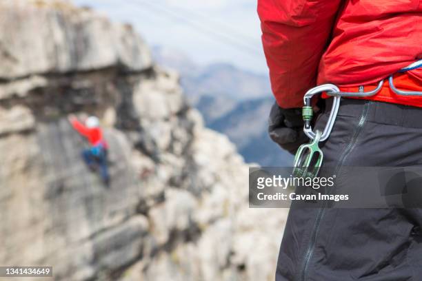 close up of carabiner hanging from belt of climber watching friend ascend rendezvous peak, wyoming, usa - カラビナ ストックフォトと画像