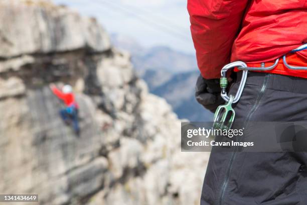 close up of carabiner hanging from belt of climber watching friend ascend rendezvous peak, wyoming, usa - karabiner stock pictures, royalty-free photos & images