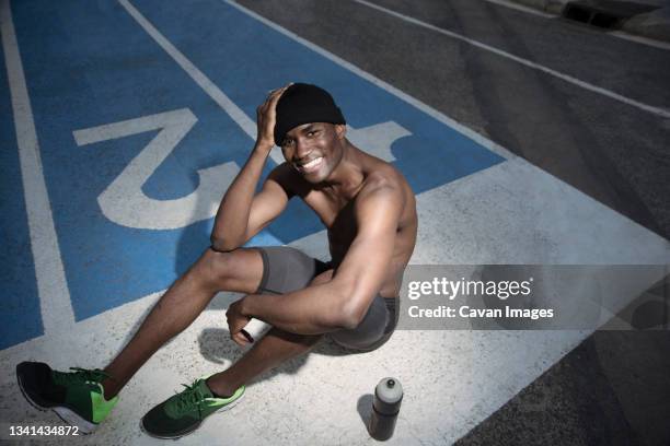 portrait of shirtless athlete sitting on all-weather running track and smiling, barcelona, spain - all weather running track stock pictures, royalty-free photos & images