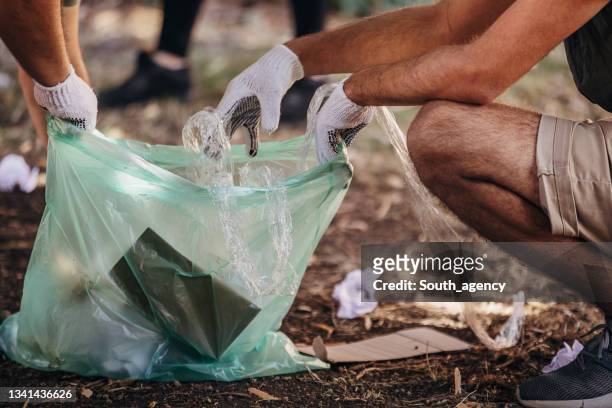 close up of volunteers picking up garbage and putting in plastic bag - nature resources and conservation agency stock pictures, royalty-free photos & images
