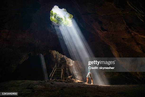 de cuerpo entero de un hombre despreocupado mirando rayos de sol entrando en la cueva. - cave fotografías e imágenes de stock