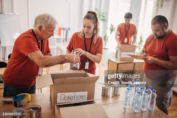 team of volunteers  in the donation center sharing and packing food,clothes,water in boxes for the people in need - philanthropist stock pictures, royalty-free photos & images