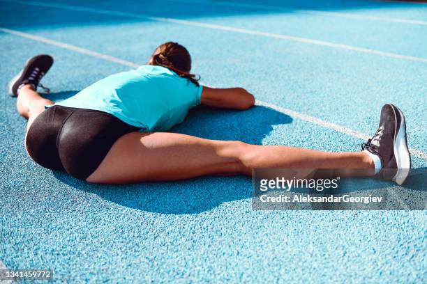 rear view of female athlete performing full split exercise for warm up before running - split acrobatiek stockfoto's en -beelden