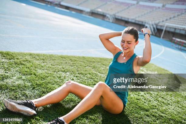 athlète féminine souriante attachant des cheveux tout en étant assise sur une piste d’athlétisme prête pour l’entraînement - short hair photos et images de collection