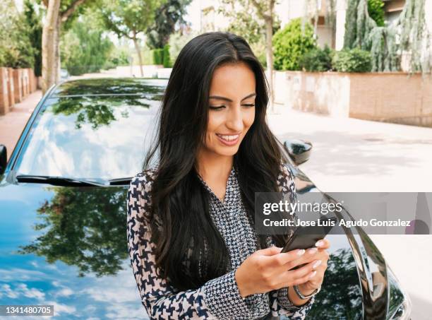 cheerful woman using smartphone near luxury car"n - auto stehend stock-fotos und bilder