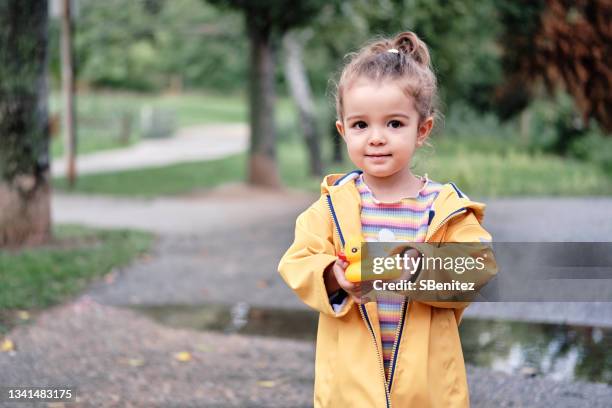 una niña de 2 años con un chubasquero amarillo está mirando a la cámara - mirando a la cámara stockfoto's en -beelden