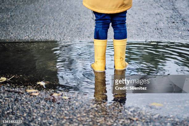 una niña está de espaldas sobre un charco - torrential rain ストックフォトと画像