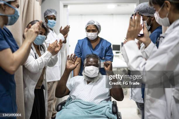 doctors and nurses celebrating senior man leaving the hospital after recovery - wearing protective face mask - leaving imagens e fotografias de stock