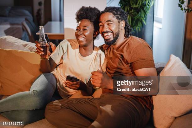 couple se relaxant sur le canapé à la maison, regardant le sport et encourageant leur équipe - couple watching tv photos et images de collection