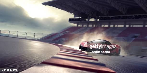 red sports car drifting around a bend on a racetrack near empty grandstand - luxury cars show stock pictures, royalty-free photos & images