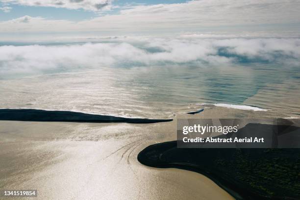 aerial shot showing a braided river flowing into the ocean between black sand beaches, iceland - nun river estuary stock-fotos und bilder