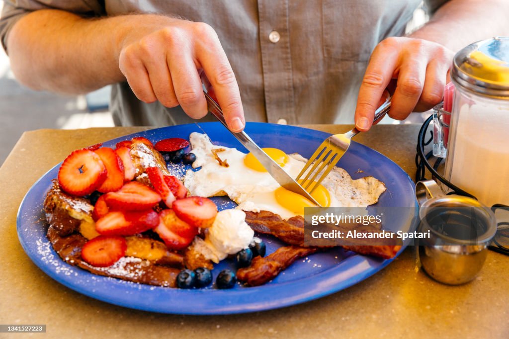 Man eating breakfast with sunny side up eggs, bacon, french toast and fresh fruits