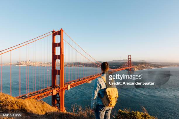 tourist with backpack looking at golden gate bridge at sunset, san francisco, california, usa - san francisco california stock pictures, royalty-free photos & images